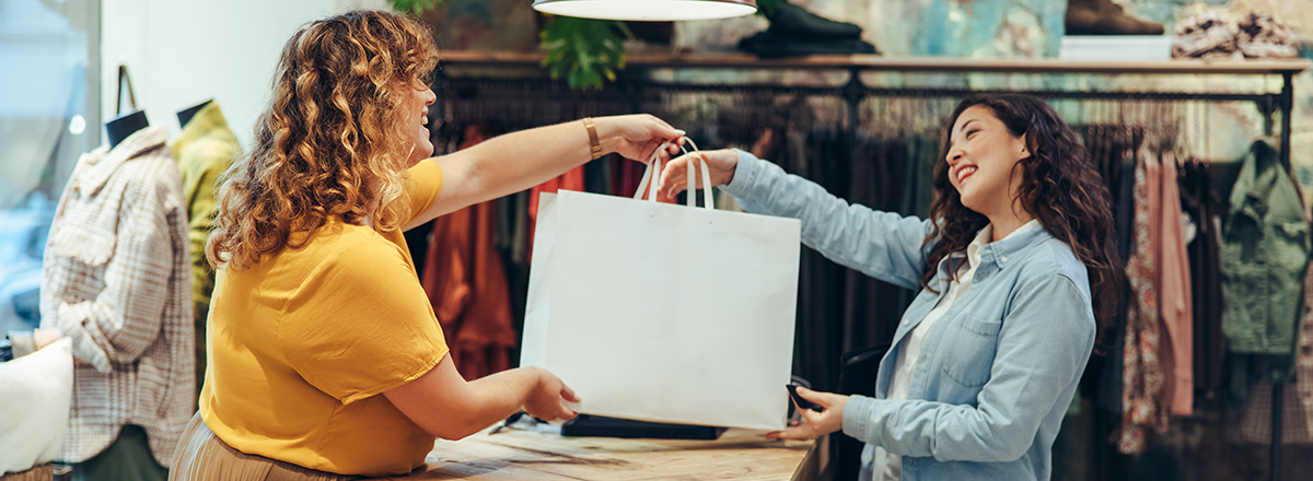 Store employee hands shopping bag to customer.