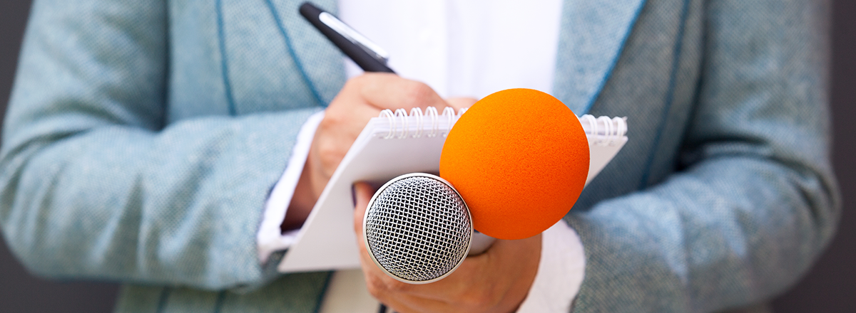 Reporter holding a microphone and taking notes on a notepad.