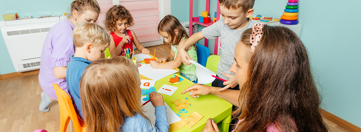 A table of children and teachers in a preschool classroom.