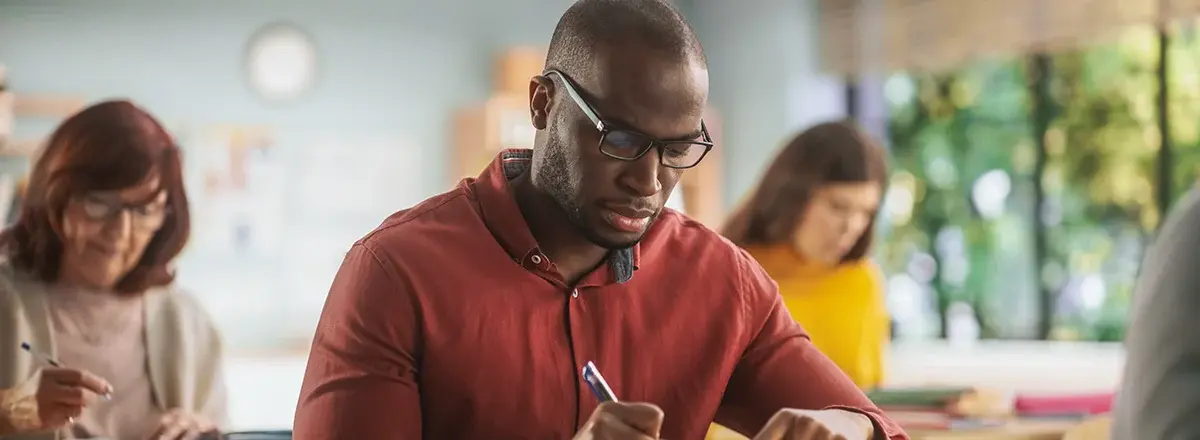 A man takes notes in a notebook during a training in a classroom.